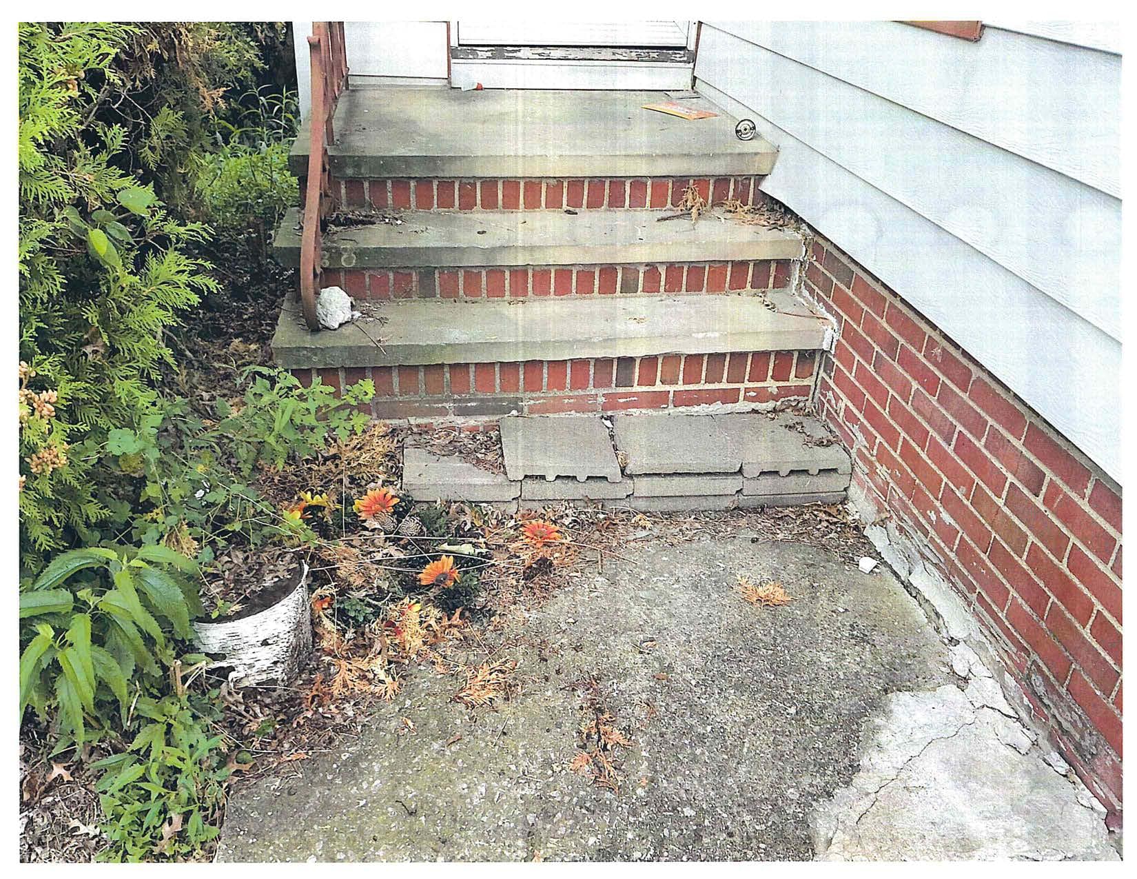 Exterior concrete steps beside a brick house, showing worn and cracked concrete near the foundation