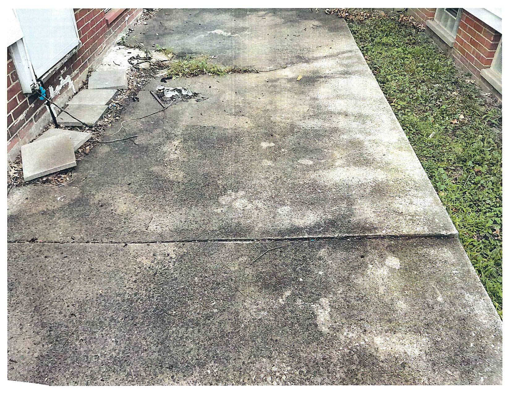 Exterior concrete walkway beside a brick house, showing cracking and uneven sections